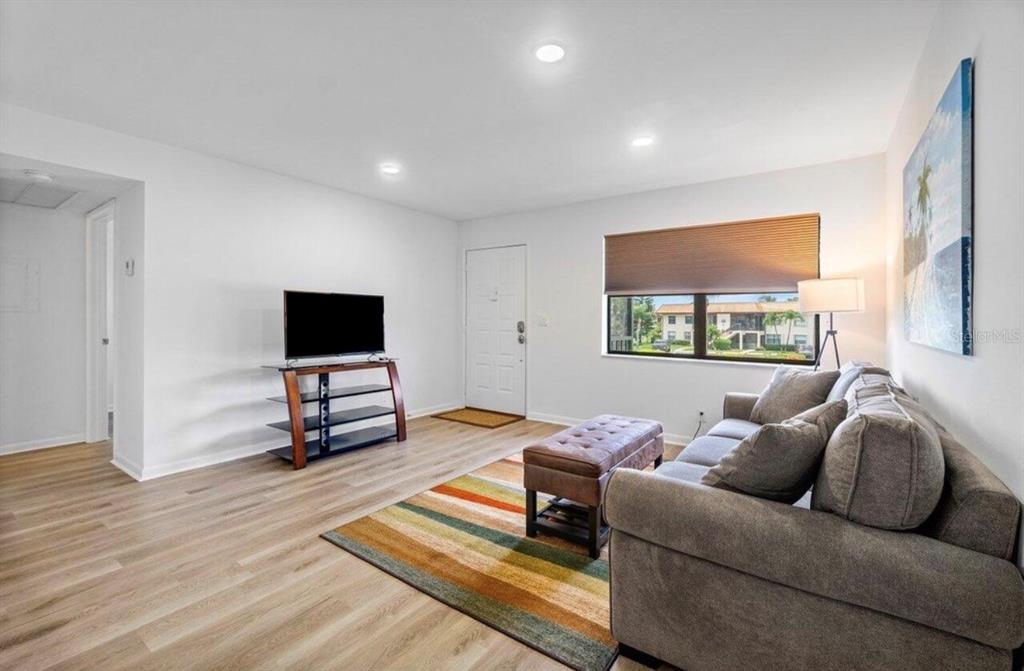 A living room with light wood flooring, a gray sofa, a television, and a striped rug — 7178 GOLF COLONY COURT UNIT 202, LAKE WORTH, FL