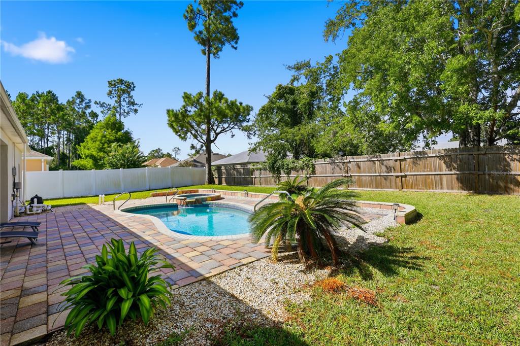 A backyard features a swimming pool with a spa, paver patio, and a wooden fence — 49 BOTANY LANE, PALM COAST, FL