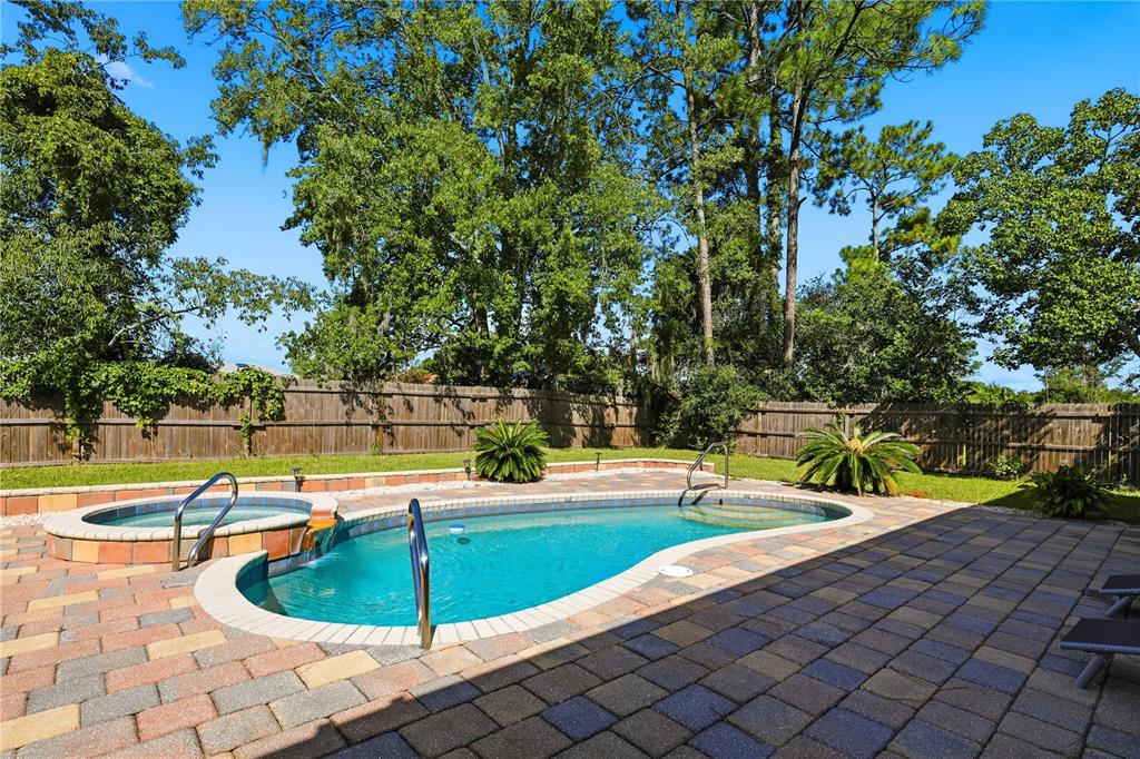 A backyard features a kidney-shaped swimming pool with an attached spa and paver patio — 49 BOTANY LANE, PALM COAST, FL