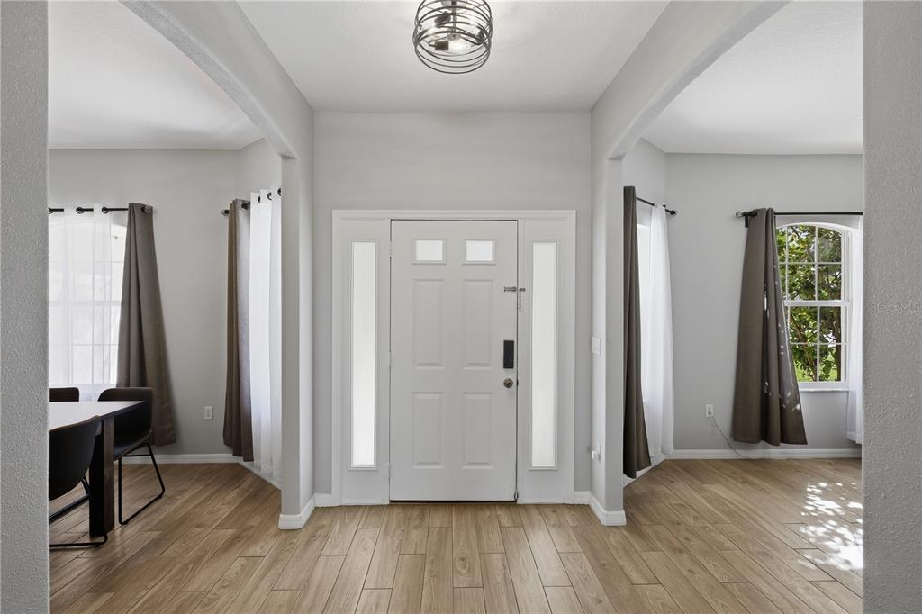 An entryway with light wood-look flooring, a white front door, and arched openings to adjacent rooms — 49 BOTANY LANE, PALM COAST, FL