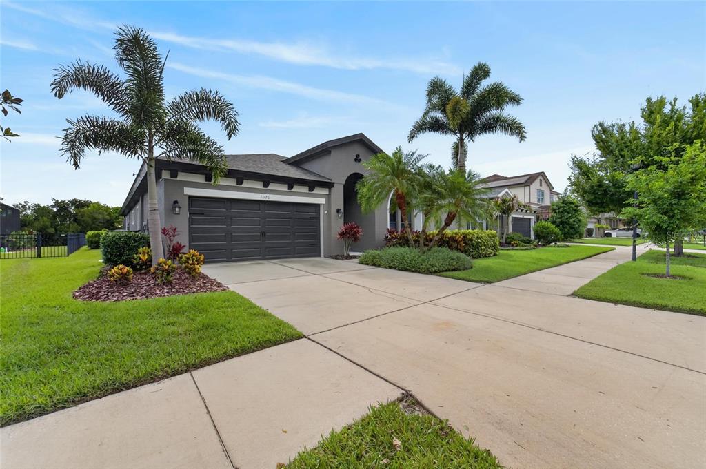 A single-story house with a gray exterior, dark garage door, and palm trees in front — 7020 OLD BENTON DRIVE, APOLLO BEACH, FL