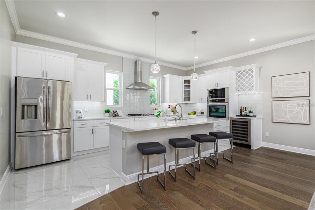 A modern kitchen features white cabinetry, stainless steel appliances, a center island, and wood flooring — 3844 SEENA MANOR COURT, TAMPA, FL