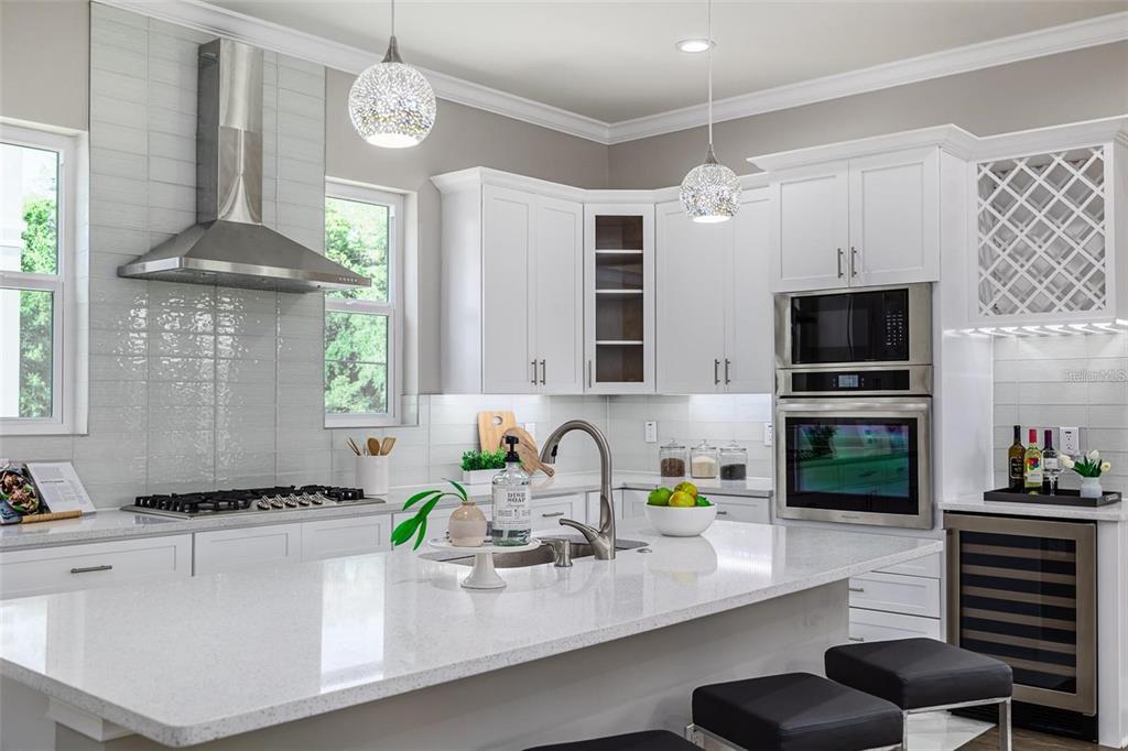 A modern kitchen features white cabinetry, a large quartz island, stainless steel appliances, and pendant lighting — 3844 SEENA MANOR COURT, TAMPA, FL