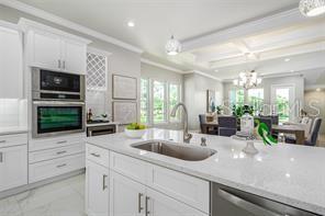 A modern white kitchen features a large island with a sink and built-in wall ovens — 3844 SEENA MANOR COURT, TAMPA, FL