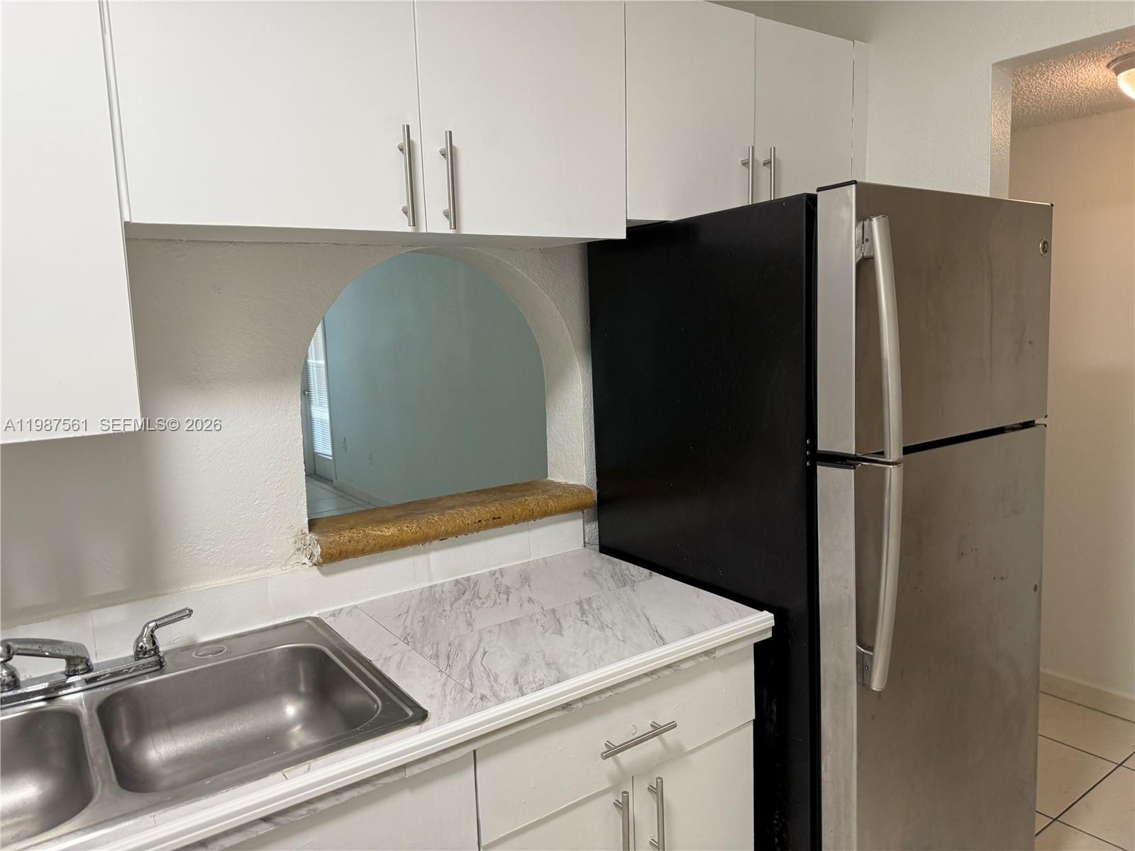 A kitchen features white cabinets, a stainless steel refrigerator, a sink, and an arched pass-through — 5755 W 20th Ave # 201, Hialeah FL 33012, HIALEAH, FL