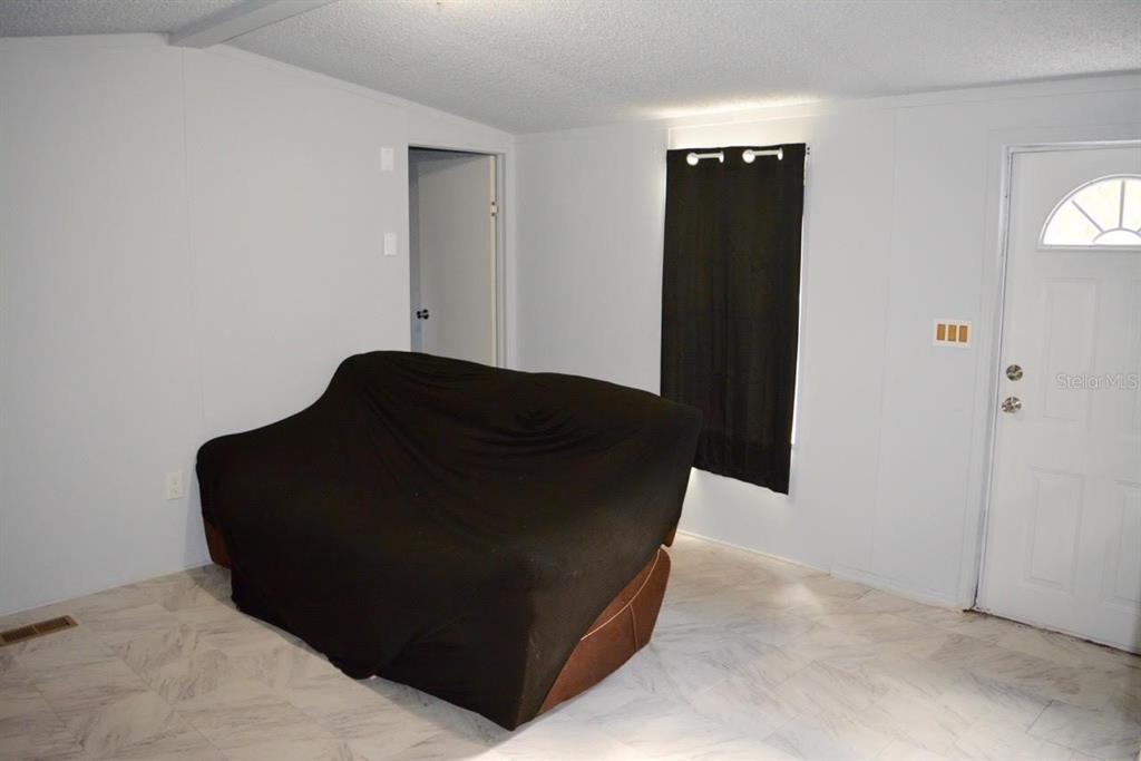 A room with white walls, light-colored tile flooring, a black sofa, and a white door — 14350 SE 41ST TERRACE, SUMMERFIELD, FL