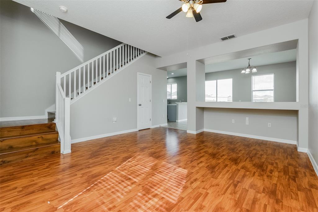 A living room with wood-look flooring, a staircase with white railings, and a kitchen pass-through window — 513 BERRY JAMES COURT, KISSIMMEE, FL