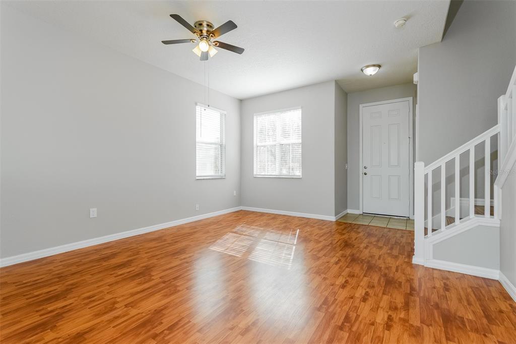 An empty living room features light gray walls, wood-look flooring, a ceiling fan, and stairs — 513 BERRY JAMES COURT, KISSIMMEE, FL