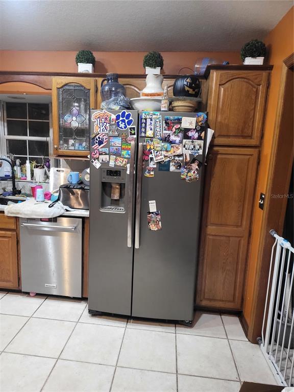 A kitchen features a stainless steel refrigerator, dishwasher, and wood cabinets with orange walls — 5491 NW OAK HILL AVENUE, ARCADIA, FL