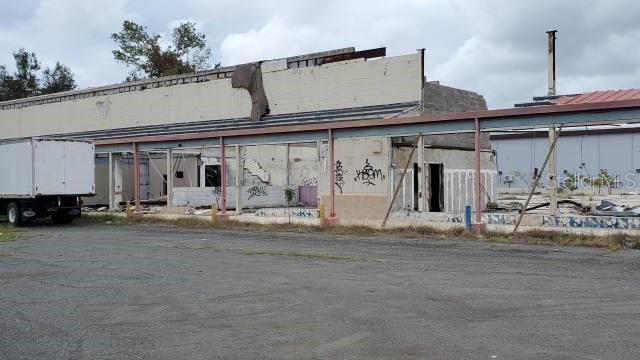 A dilapidated commercial building with a covered walkway and graffiti stands in a paved lot — PR-116 INT. PR-121, YAUCO, PR