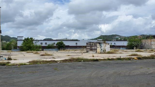 A large, vacant concrete lot sits in front of a long, single-story commercial building — PR-116 INT. PR-121, YAUCO, PR