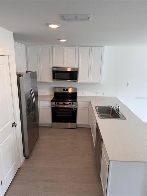A kitchen features white cabinets, stainless steel appliances, and a light-colored countertop island — 1231 ORION ST, DAVENPORT, FL