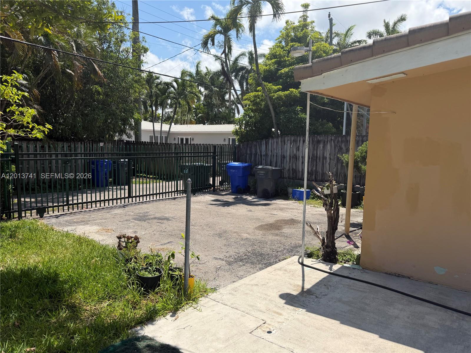An outdoor paved area features a metal fence, several trash bins, and a building corner — HOLLYWOOD, FL