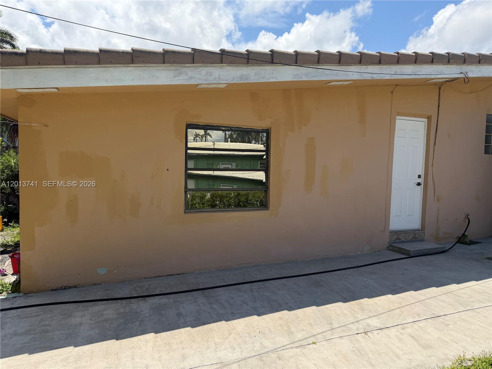 The exterior of a tan building features a single window and a white door — HOLLYWOOD, FL