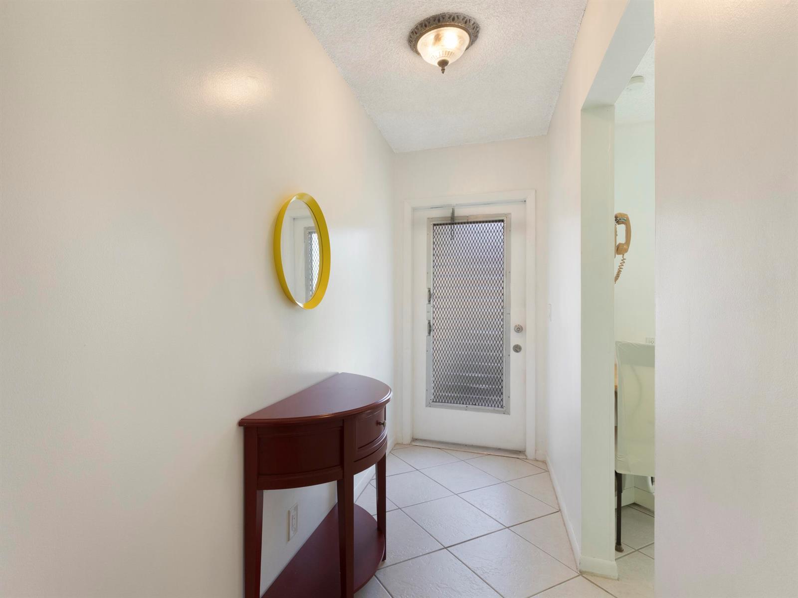 A tiled entryway features a semi-circular console table, a yellow-framed mirror, and a screen door — 857 Worcester Lane # B, Lake Worth FL 33467, LAKE WORTH, FL