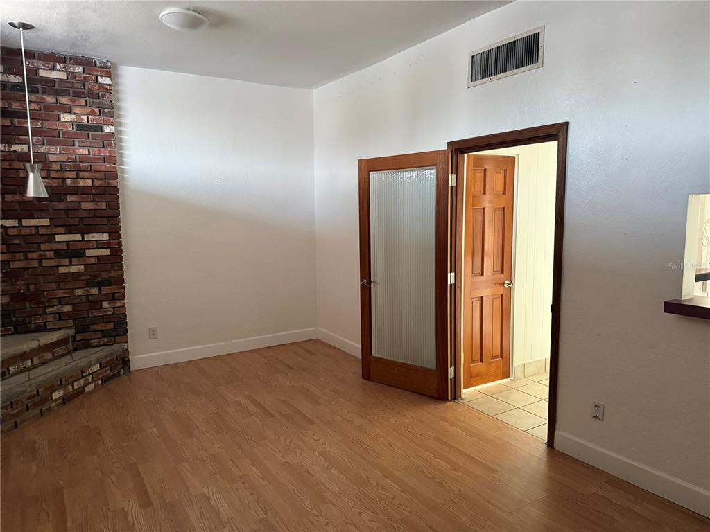 A room with wood flooring, a brick fireplace, and a door leading to another room — 4930 PARK BOULEVARD N UNIT 1, PINELLAS PARK, FL