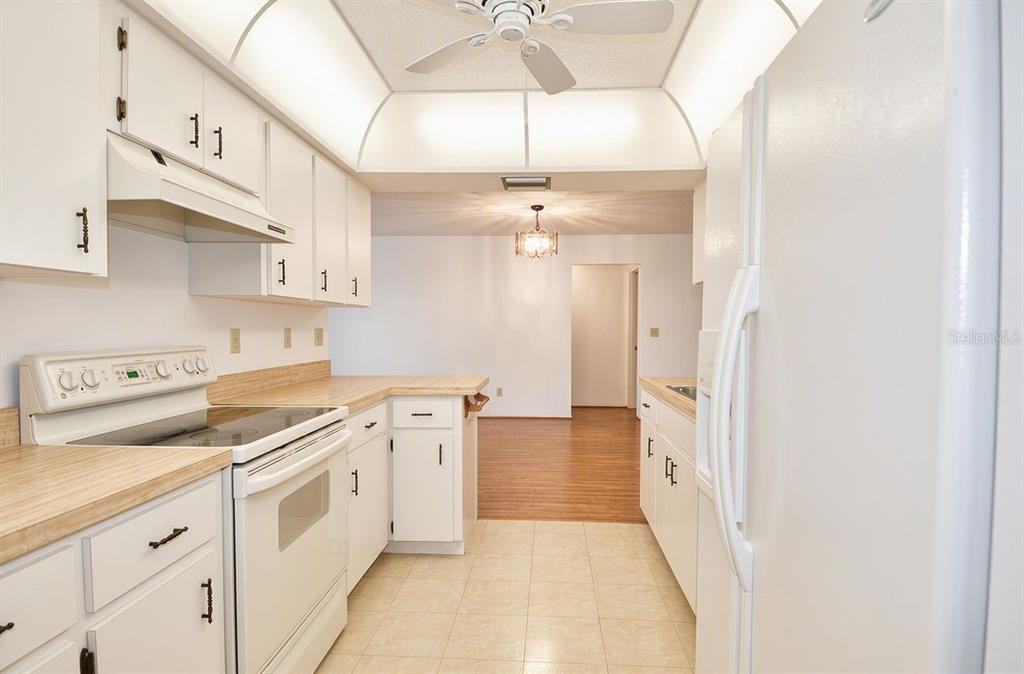 A kitchen with white cabinets, laminate countertops, and white appliances opens to a dining area — 1379 EVEREST ROAD, VENICE, FL