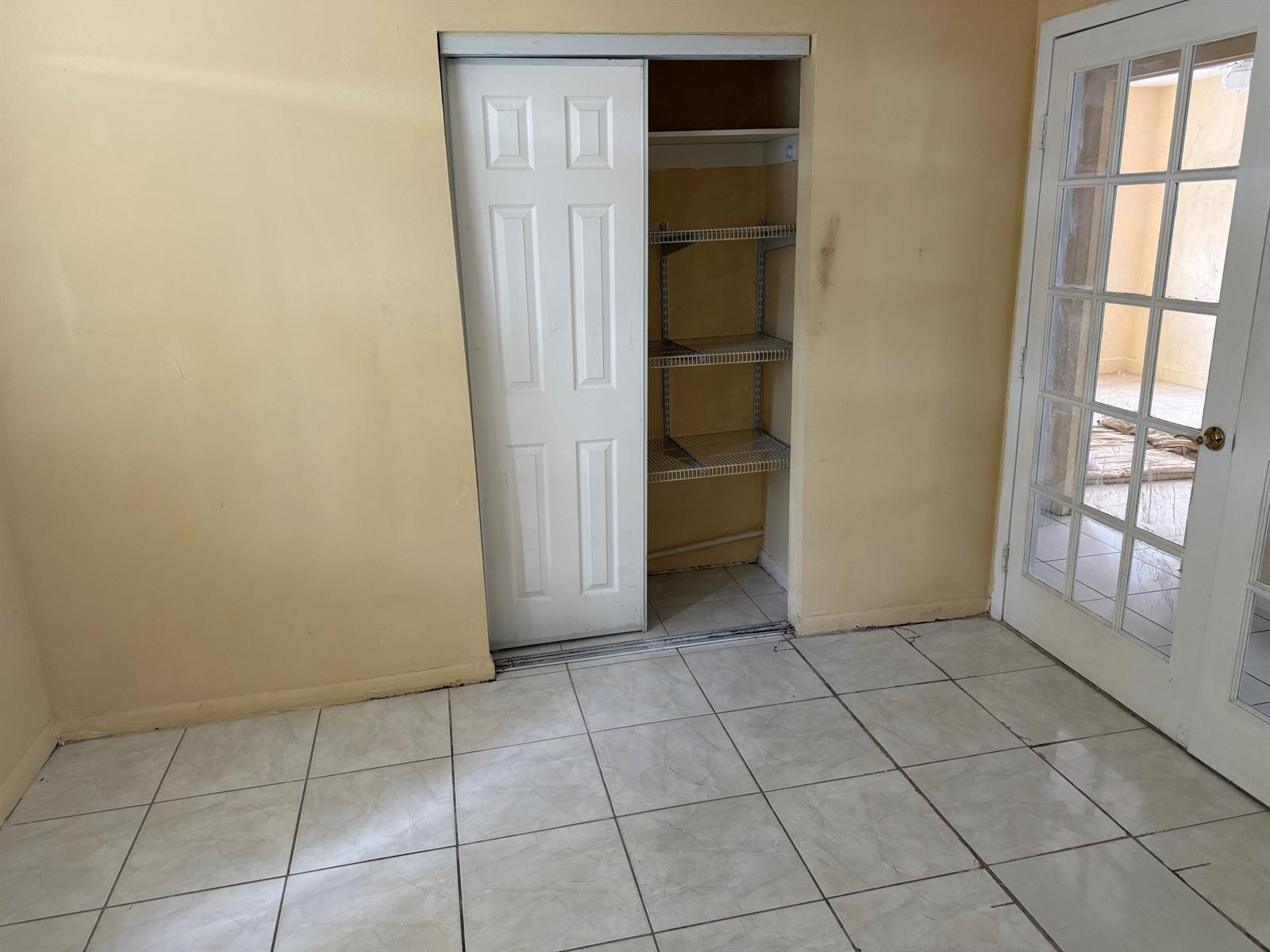 A room with yellow walls, tiled floors, a closet with wire shelving, and a glass door — 1676 W 10th Street, Riviera Beach FL 33404, RIVIERA BEACH, FL