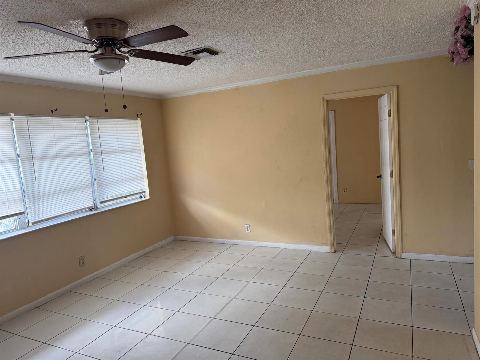 An empty room with beige walls, white tile flooring, a ceiling fan, and a doorway — 1676 W 10th Street, Riviera Beach FL 33404, RIVIERA BEACH, FL