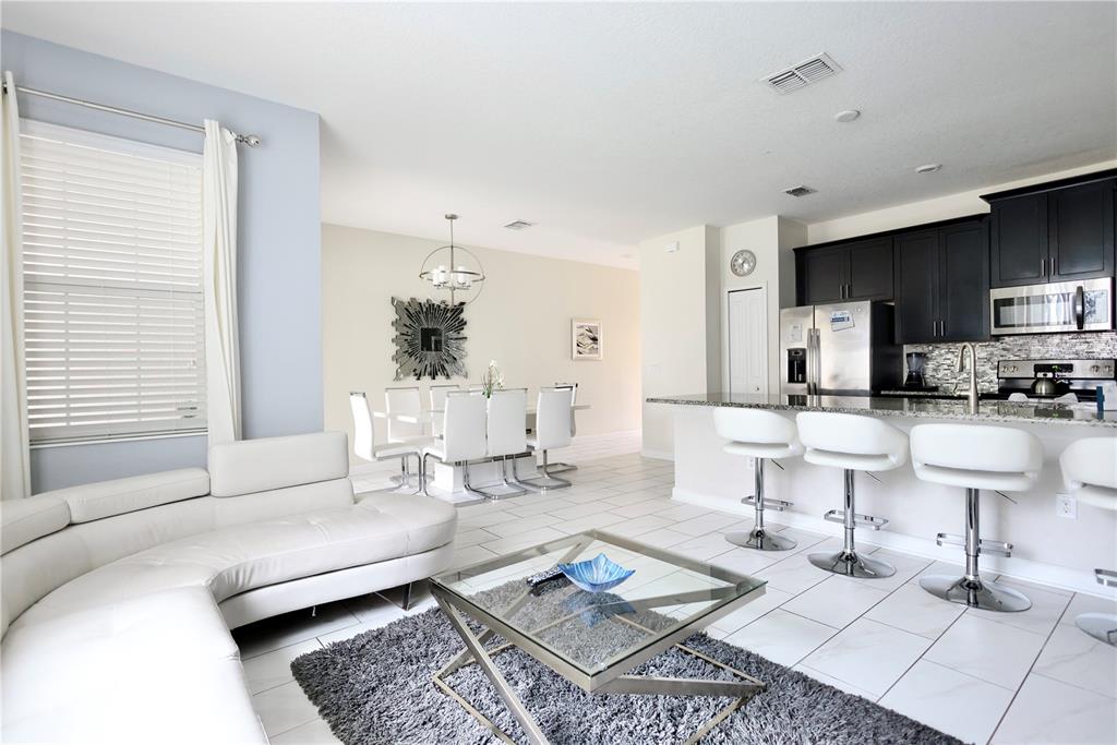An open-concept living room and kitchen feature white tile floors, a sectional, and bar seating — 9063 DOGLEG DRIVE, DAVENPORT, FL