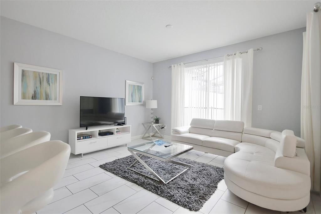 A living room features white tile floors, a white sectional sofa, and a glass coffee table — 9063 DOGLEG DRIVE, DAVENPORT, FL