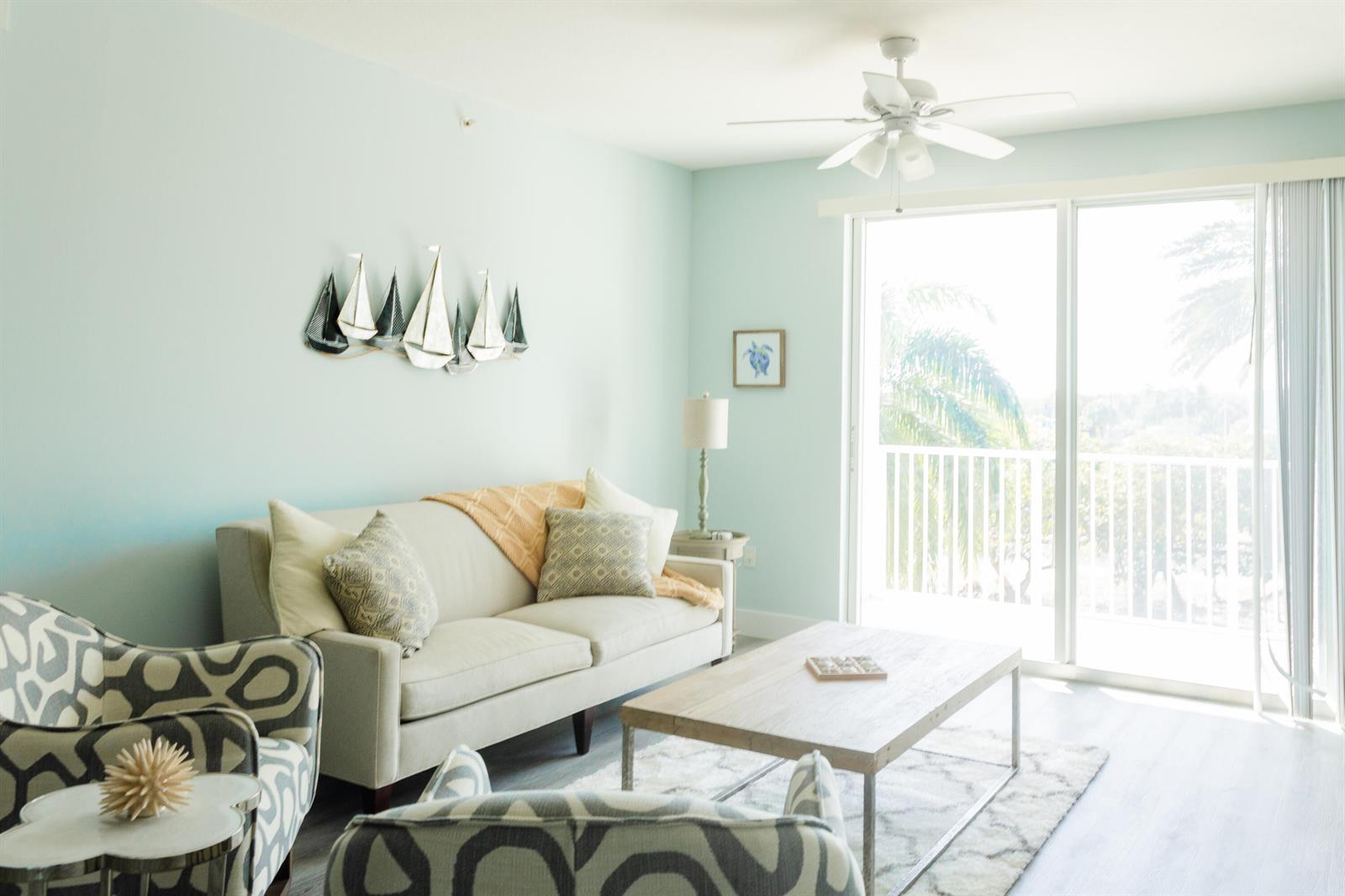 A living room features a light-colored sofa, patterned armchairs, a coffee table, and wall decor — 802 W Windward Way # 311, Lantana FL 33462, LANTANA, FL
