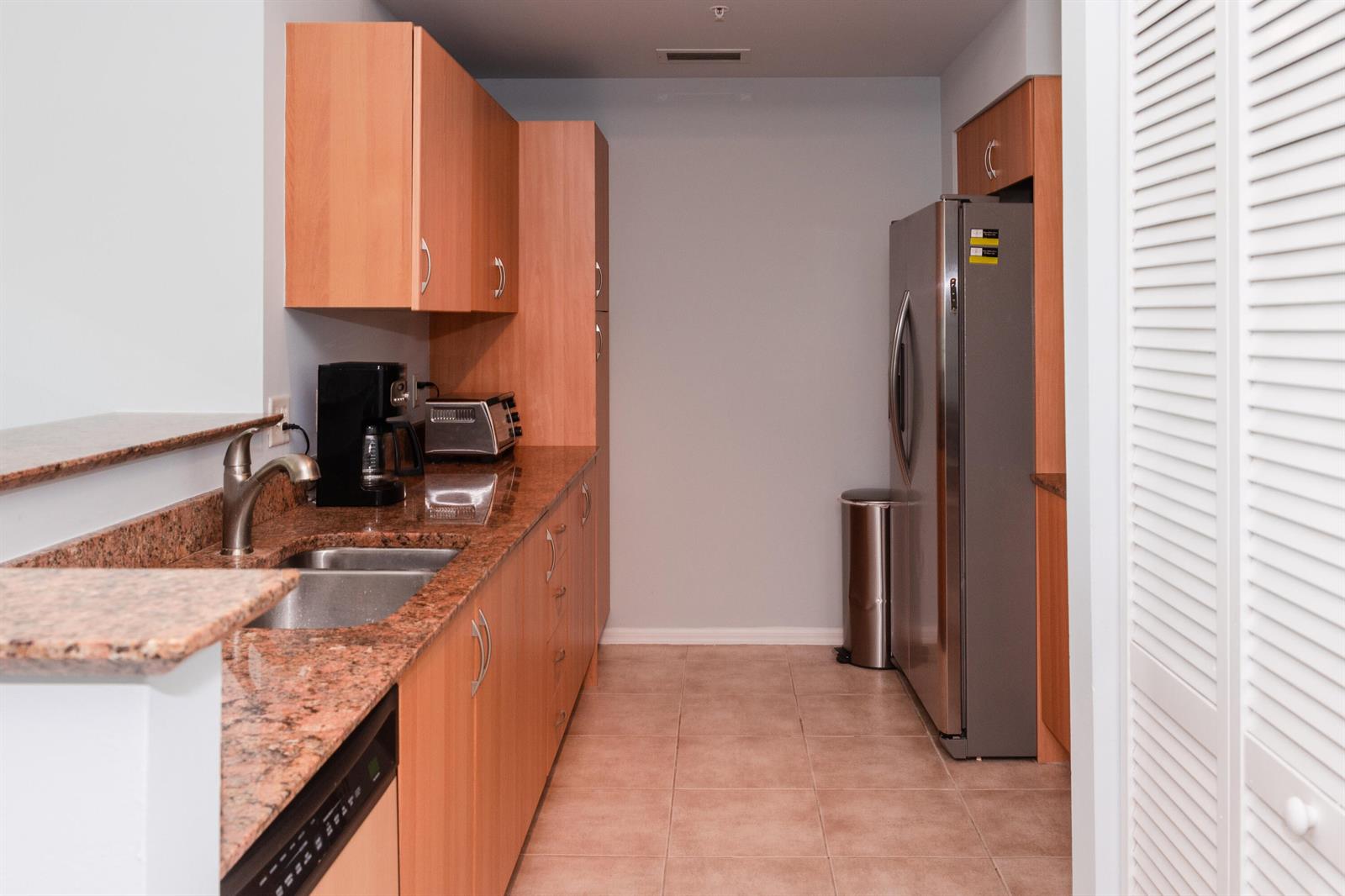 A kitchen features light wood cabinets, granite countertops, stainless steel appliances, and tile flooring — 802 W Windward Way # 311, Lantana FL 33462, LANTANA, FL