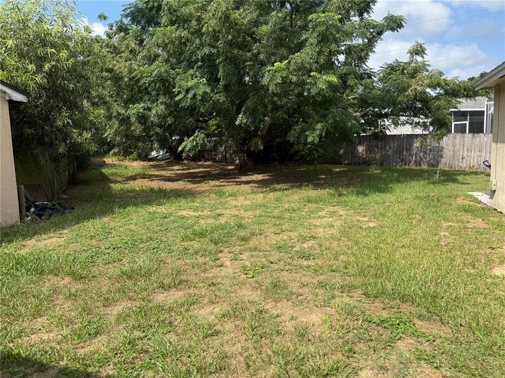 A grassy backyard features a large tree, a wooden fence, and parts of two houses — 7425 VILLAS OAK COURT, ORLANDO, FL