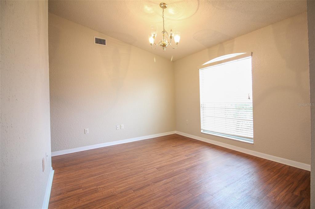 An empty room features wood-look flooring, beige walls, a chandelier, and a single window — 3002 CHASEWOOD DRIVE, LAKELAND, FL