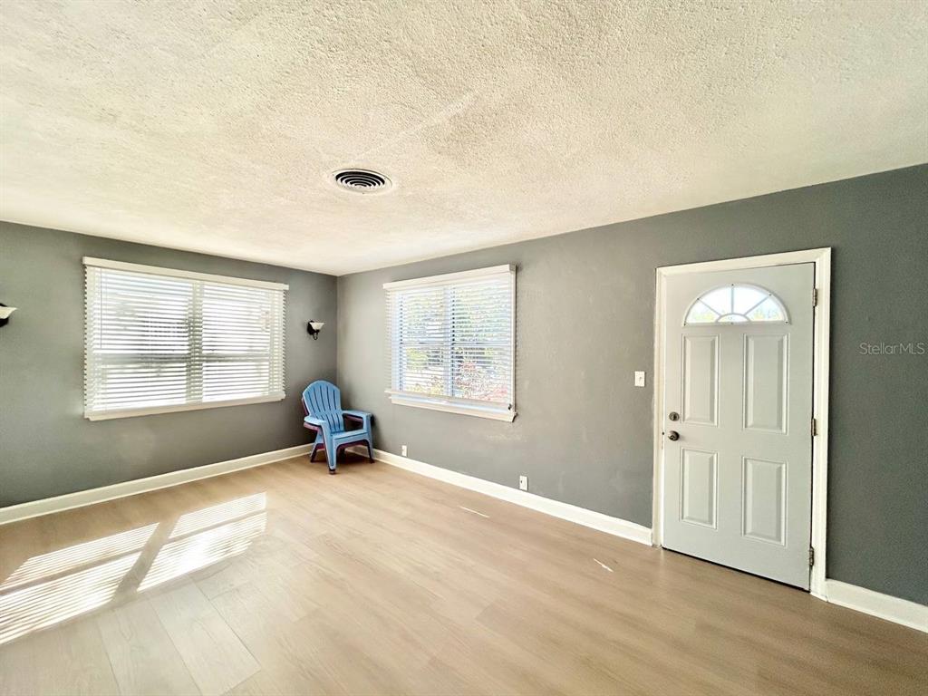 An empty room features gray walls, light wood-look flooring, two windows, and a white door — 2720 EDWARDS AVENUE S, ST PETERSBURG, FL