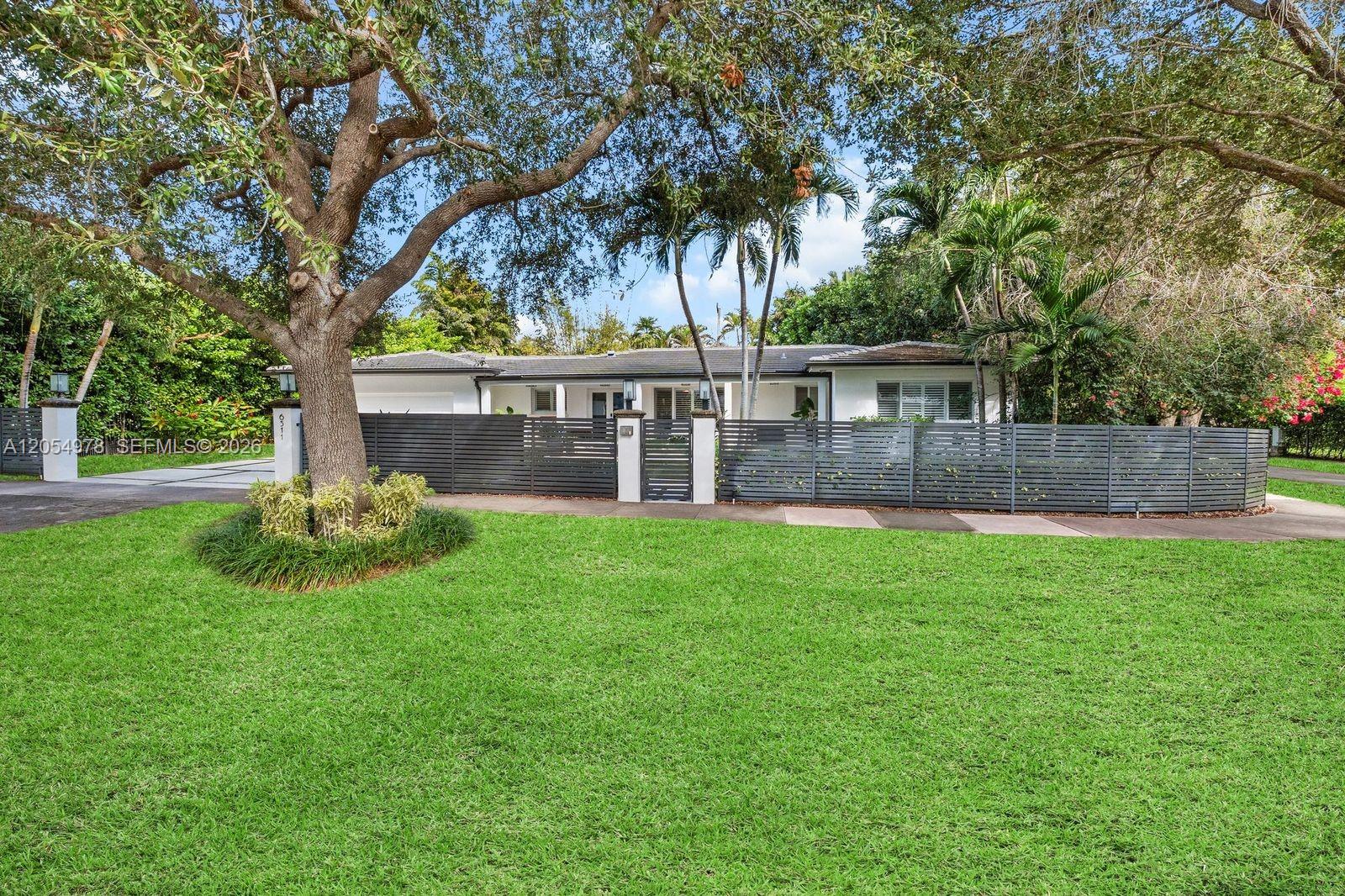 A single-story house with a white exterior sits behind a dark horizontal slat fence — 6511 Riviera Dr, Coral Gables FL 33146, CORAL GABLES, FL
