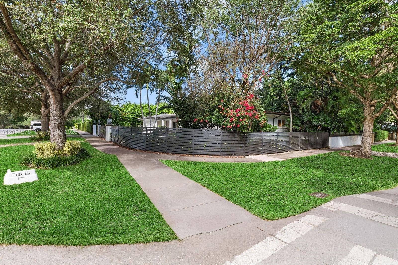 A house exterior is partially obscured by a dark horizontal fence and mature trees — 6511 Riviera Dr, Coral Gables FL 33146, CORAL GABLES, FL