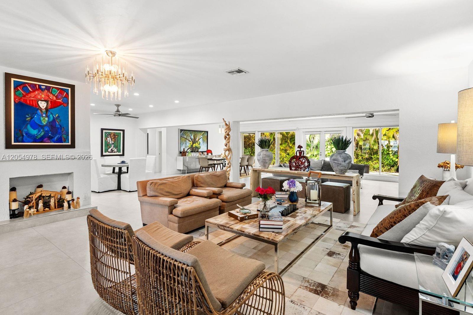 A bright, open-concept living room features a fireplace, wicker chairs, and a large coffee table — 6511 Riviera Dr, Coral Gables FL 33146, CORAL GABLES, FL