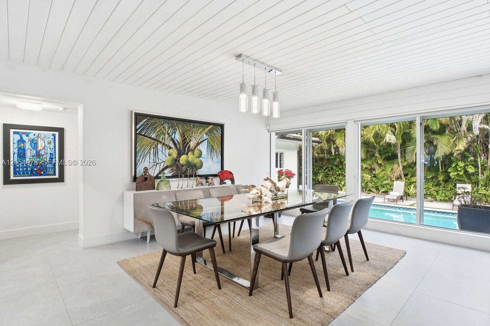 A modern dining room features a glass table, gray chairs, and a view of a pool — 6511 Riviera Dr, Coral Gables FL 33146, CORAL GABLES, FL