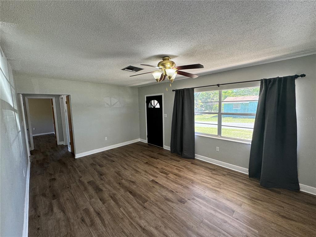 A living room features wood-look flooring, a ceiling fan, a black front door, and windows — 460 MOUNT VERNON COURT, EUSTIS, FL
