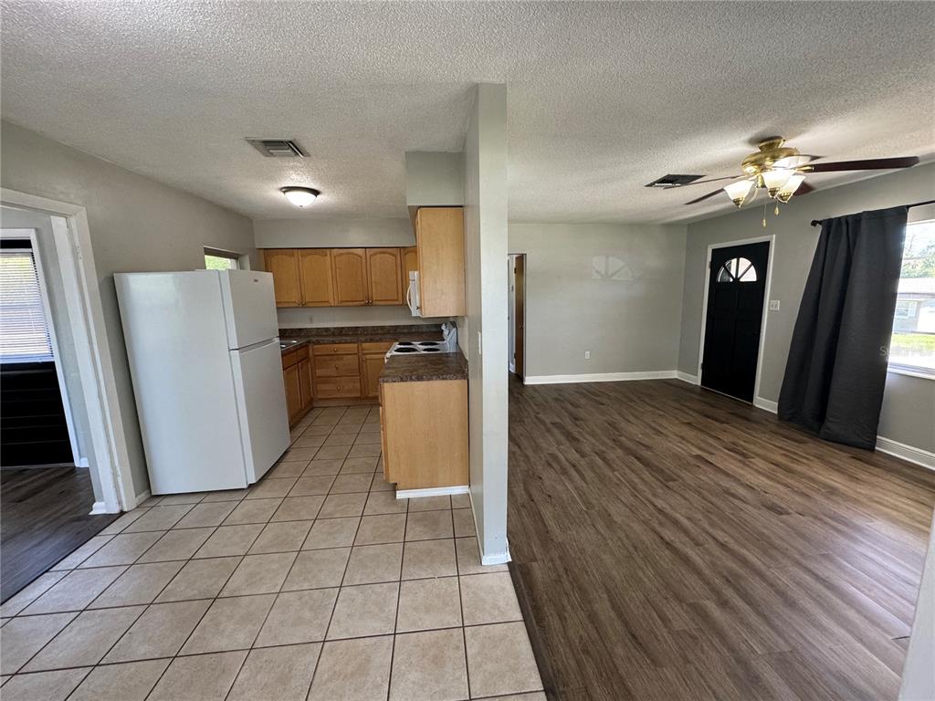 A kitchen with tile floors and wood cabinets opens into a living area with wood-look flooring — 460 MOUNT VERNON COURT, EUSTIS, FL