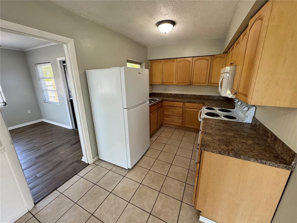 A kitchen with light wood cabinets, dark countertops, and tile flooring next to a dining area — 460 MOUNT VERNON COURT, EUSTIS, FL