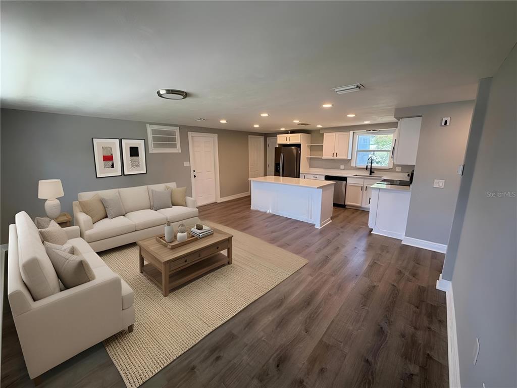 An open-concept living room and kitchen featuring white cabinetry, a central island, and wood flooring — 3511 CAMBRIDGE STREET, NEW PORT RICHEY, FL