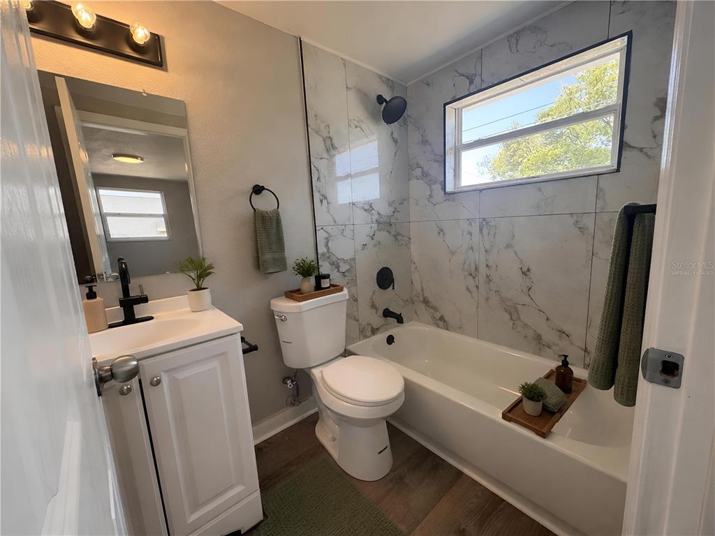 A bathroom features a white vanity, a toilet, and a bathtub with marble-patterned tile walls — 3511 CAMBRIDGE STREET, NEW PORT RICHEY, FL