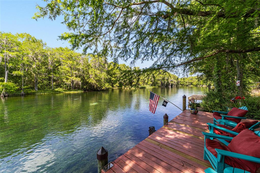 A wooden dock with turquoise chairs overlooks a clear river surrounded by lush green trees — 11144 SW 190TH AVENUE, DUNNELLON, FL