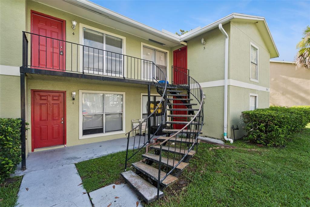A two-story apartment building exterior features red doors, a metal spiral staircase, and green siding — 1847 CARALEE BOULEVARD UNIT 4, ORLANDO, FL