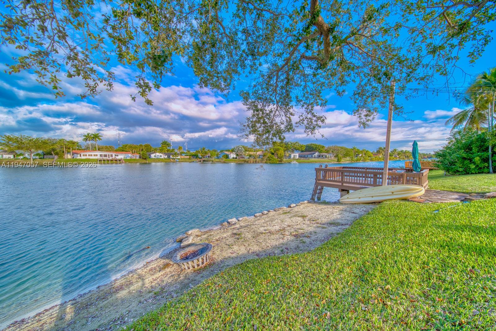 A grassy backyard leads to a small sandy beach, a wooden dock, and a lake — 12620 SW 114th Ave, Miami FL 33176, MIAMI, FL