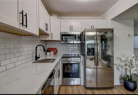 A kitchen features white cabinets, stainless steel appliances, a subway tile backsplash, and quartz countertops — 2500 HARN BLVD UNIT F22, CLEARWATER, FL