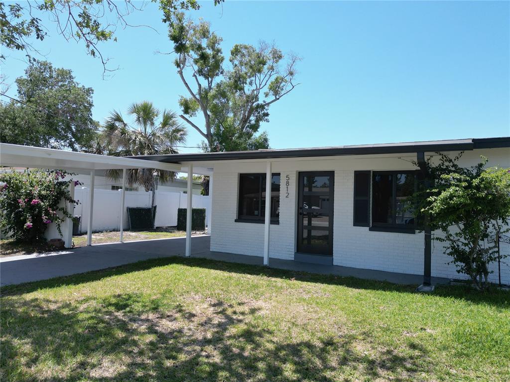 A white brick house features a flat roof, a carport, and a glass-paneled front door — 5812 LIVERPOOL DRIVE, TAMPA, FL