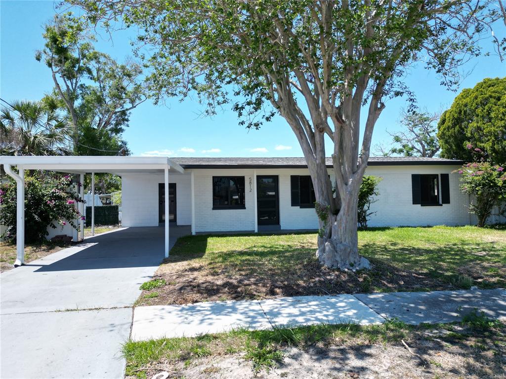 A single-story white brick house features a carport, a large tree, and a front lawn — 5812 LIVERPOOL DRIVE, TAMPA, FL