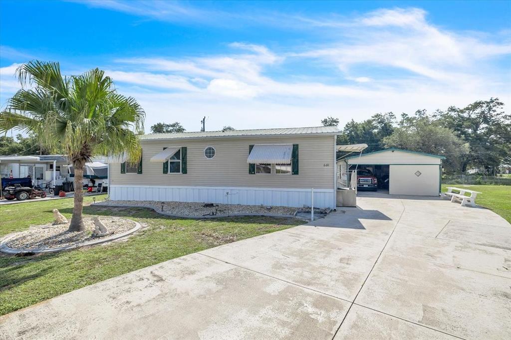A tan mobile home with a metal roof, attached carport, and concrete driveway — 6801 BERNADEAN BOULEVARD, PUNTA GORDA, FL