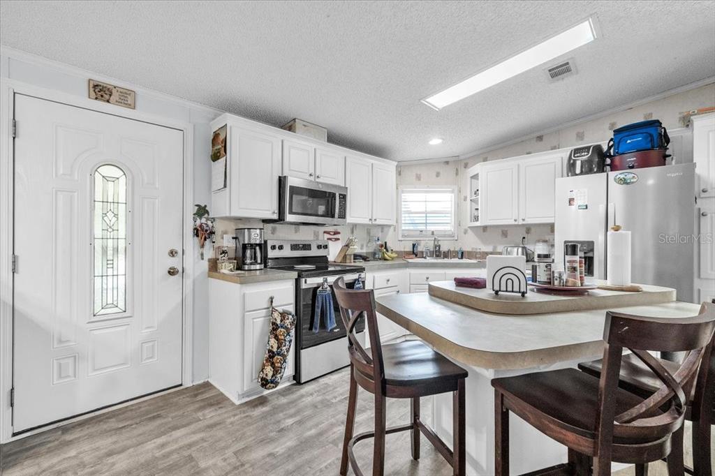 A kitchen features white cabinets, stainless steel appliances, a center island, and wood-look flooring — 6801 BERNADEAN BOULEVARD, PUNTA GORDA, FL