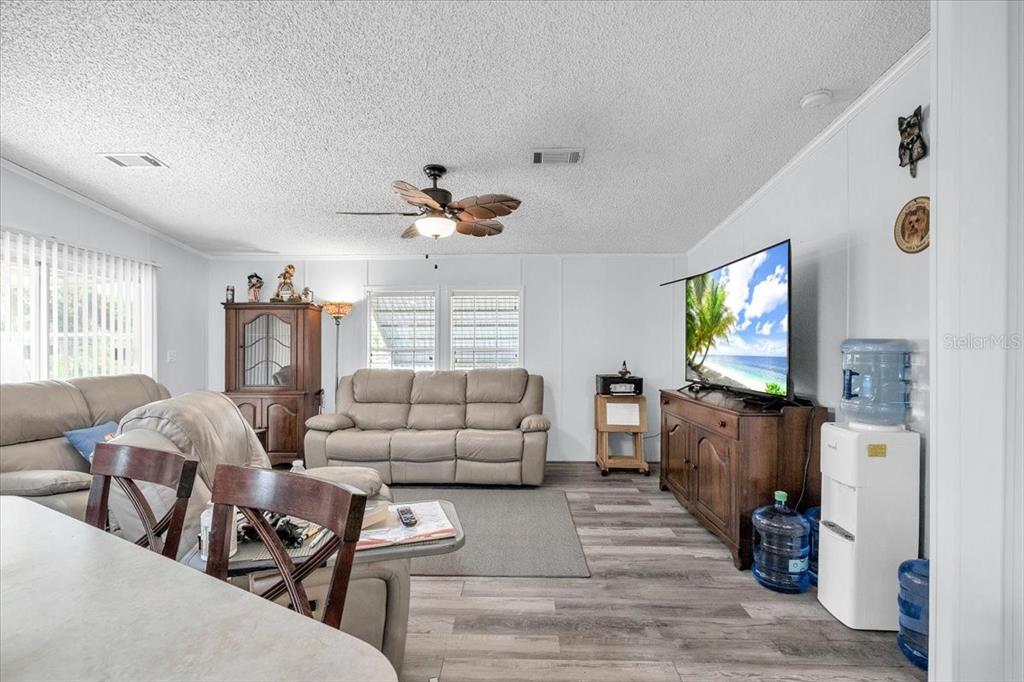 A living room features light wood-look flooring, a ceiling fan, and a wall-mounted television — 6801 BERNADEAN BOULEVARD, PUNTA GORDA, FL