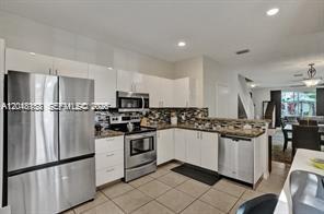 A modern kitchen features white cabinets, stainless steel appliances, and light-colored tile flooring — 3901 San Simeon Ln, Weston FL 33331, WESTON, FL