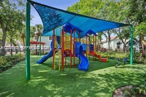 A colorful playground structure sits under a large blue shade canopy on a grassy lawn — 3901 San Simeon Ln, Weston FL 33331, WESTON, FL
